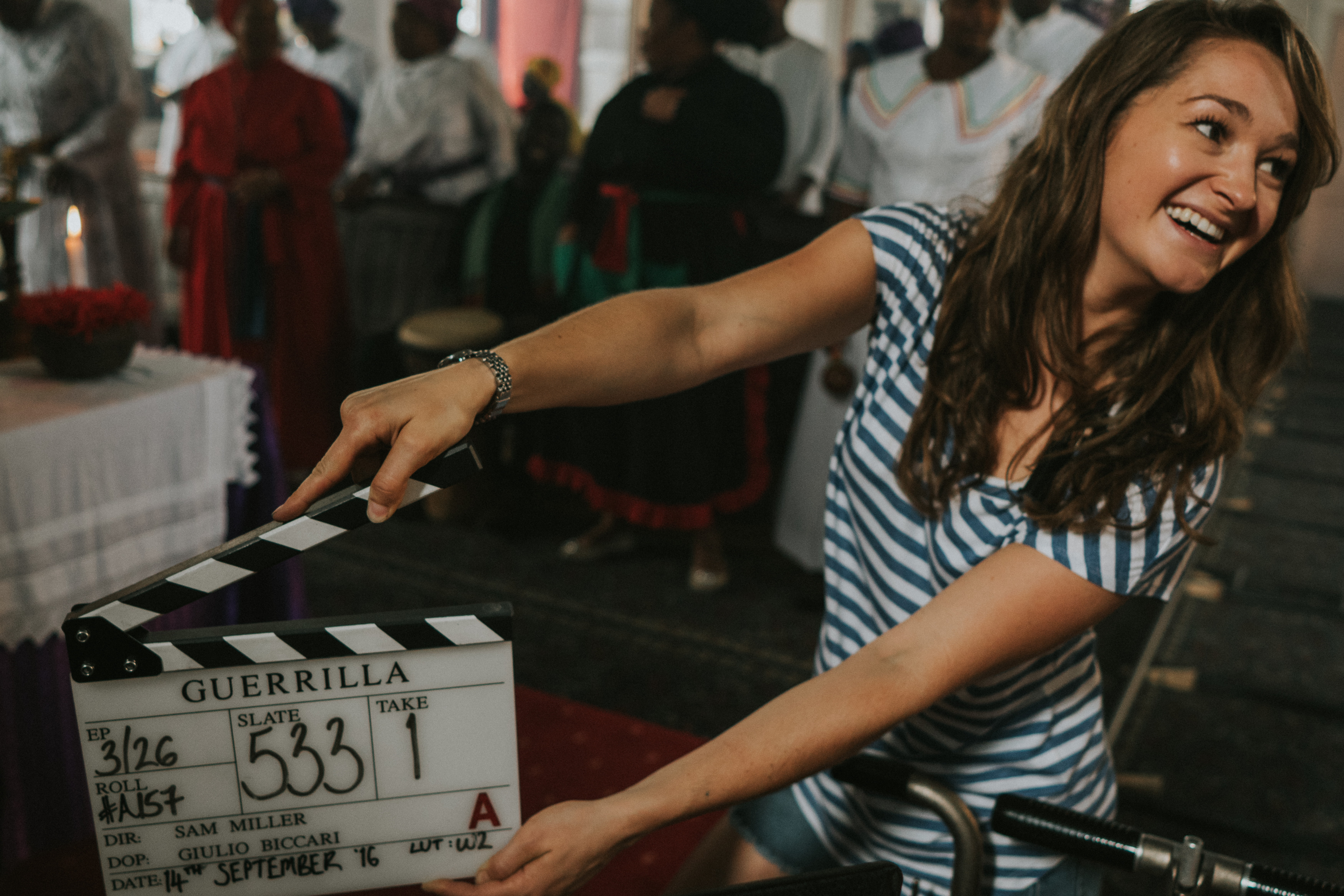 Behind-the-scenes image of a woman smiling while holding a clapper board on the set of the movie Guerilla