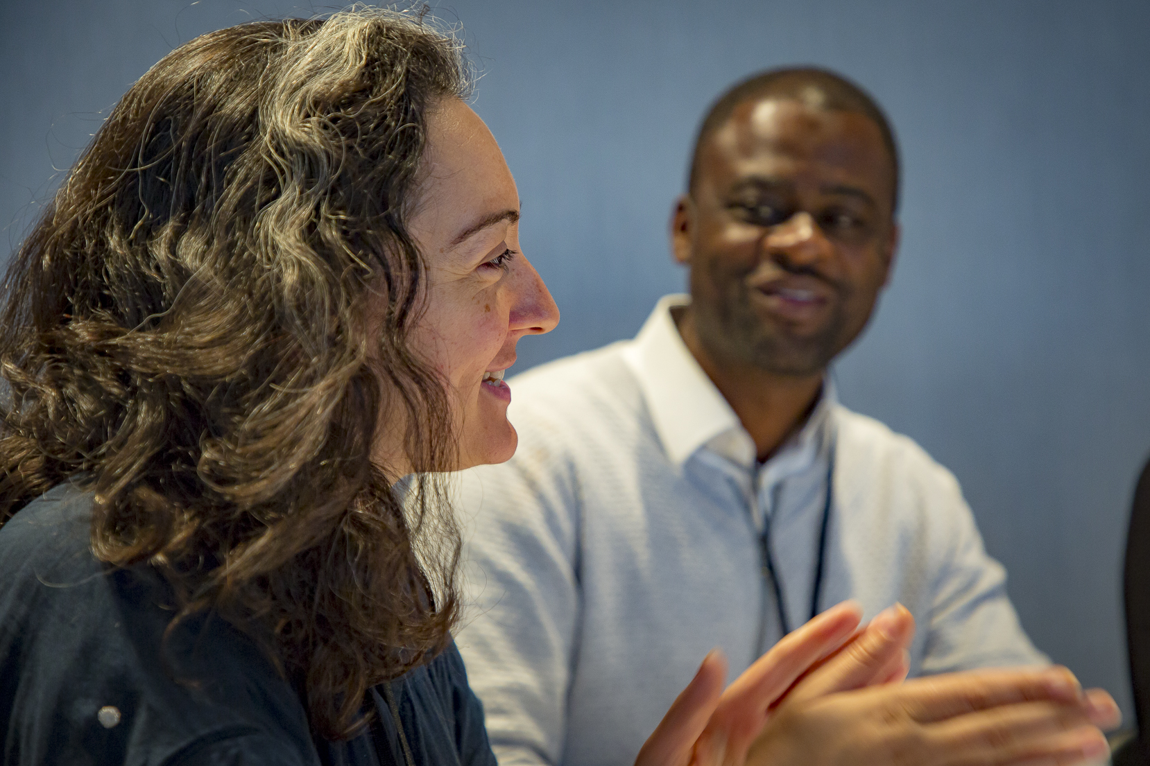 Woman in the foreground speaking and motioning with hands and a man in the background watching