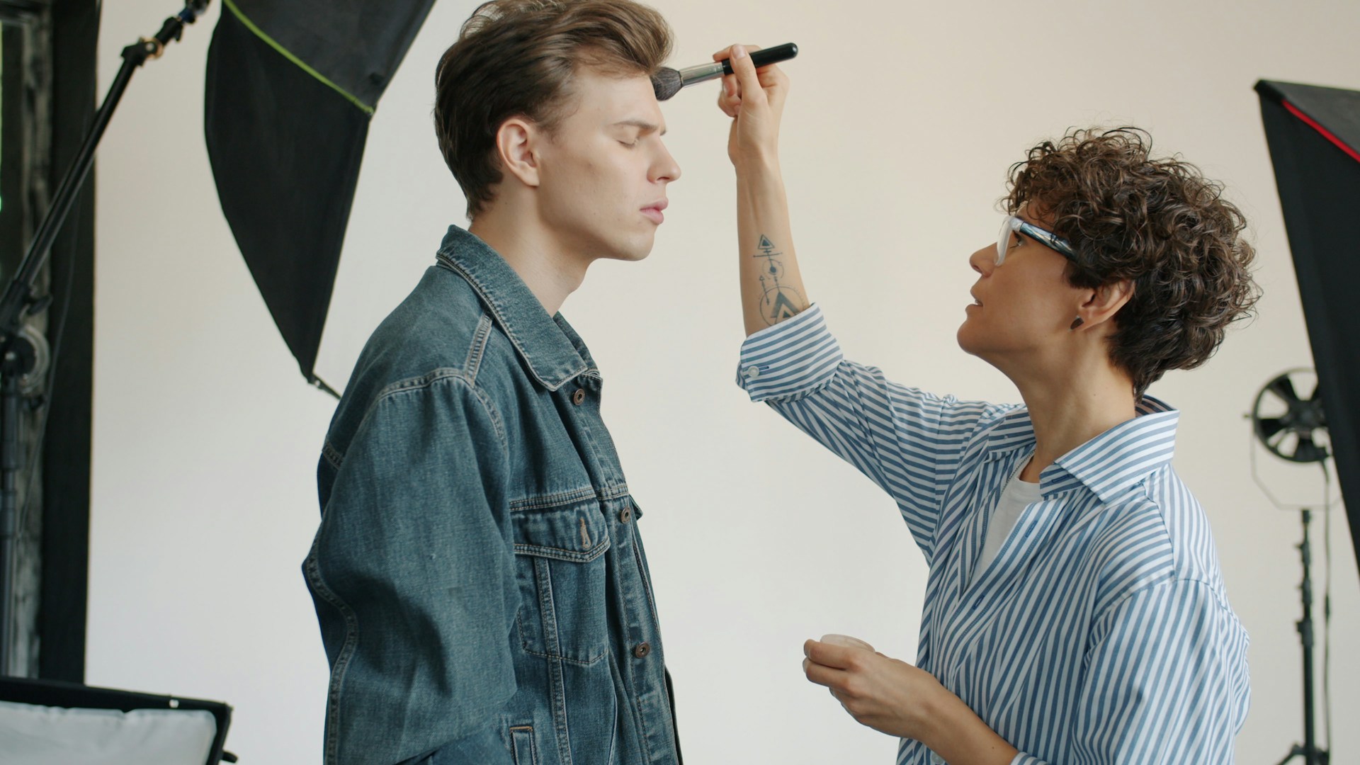 A make-up artist applies make-up to another person on set