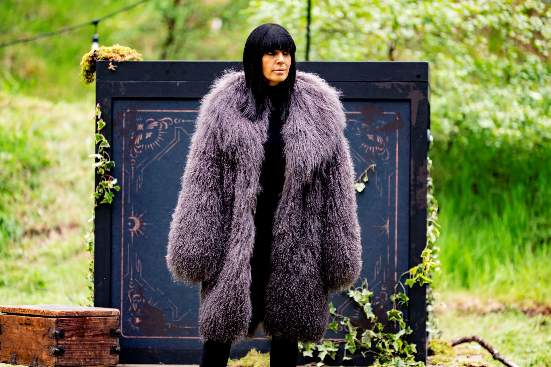 Claudia Winkleman standing on the set of The Traitors wearing a large faux fur coat