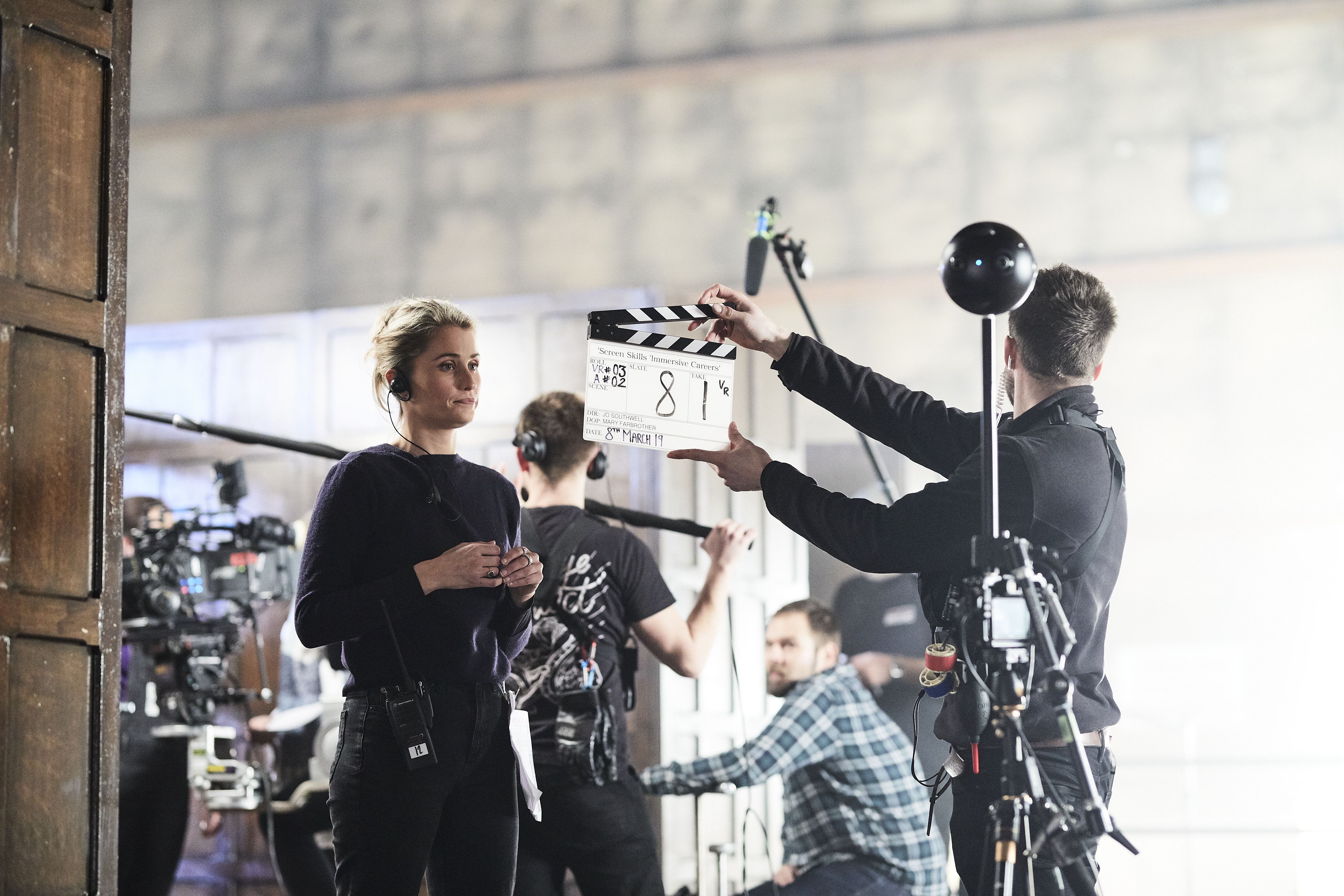 Man with clapper board stands in front of a woman wearing a headset with a 360 camera rig in the foreground