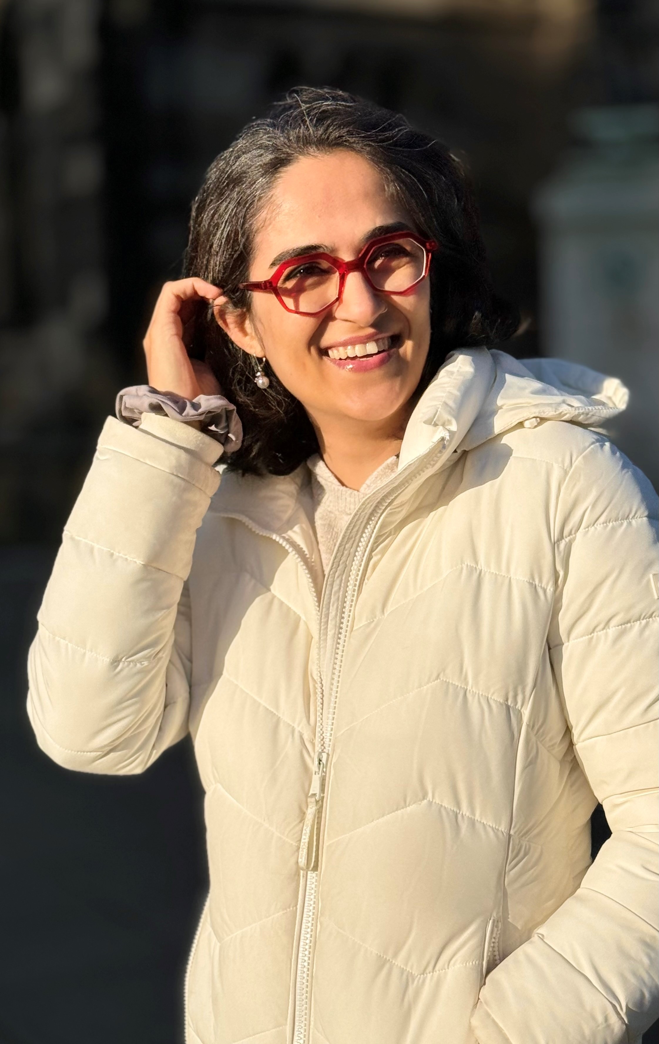 Elahe Esmaili stands smiling in a white coat with her arm raised to push back hair