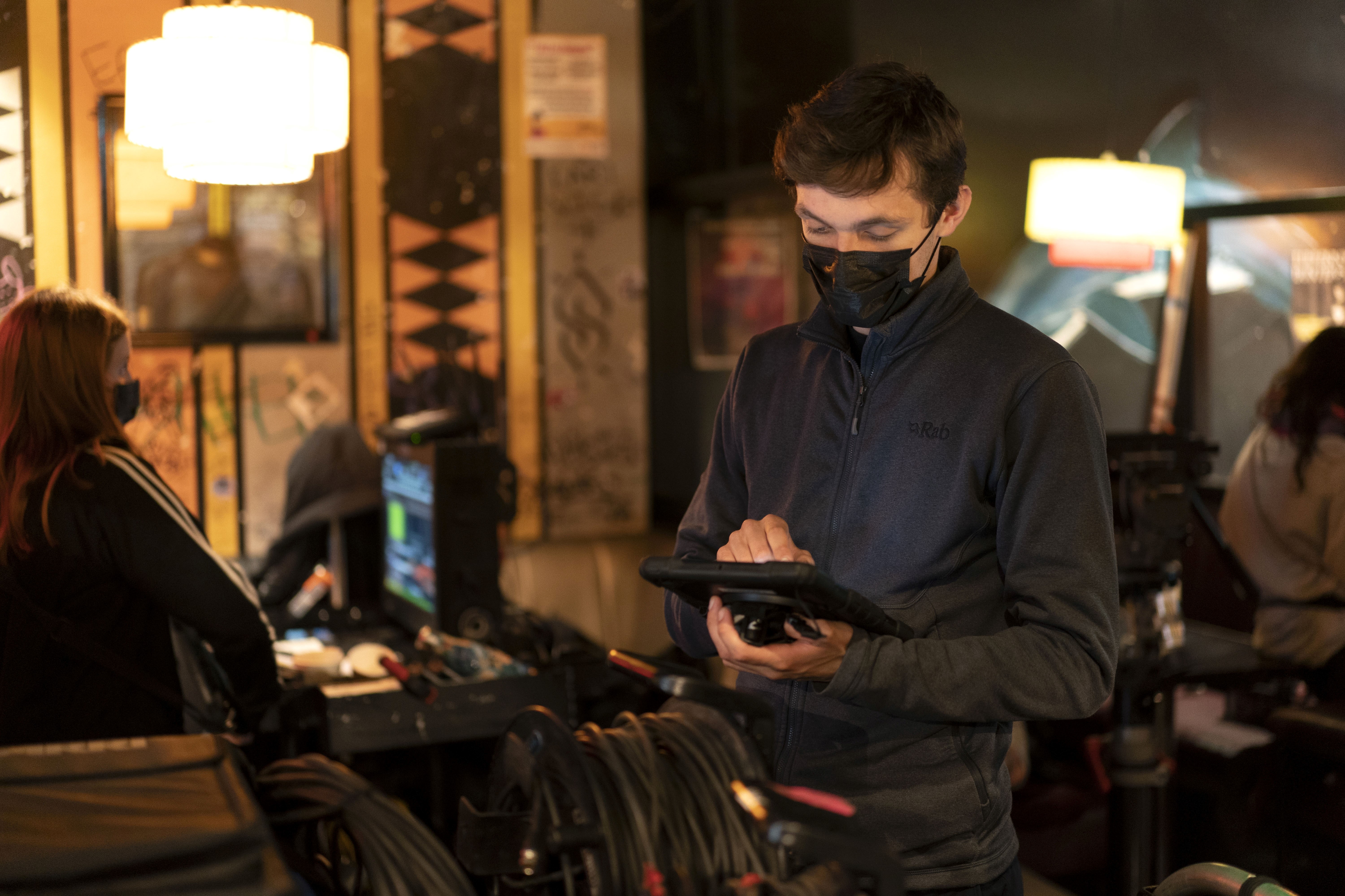 A crew member is standing up holding a tablet while wearing a face mask