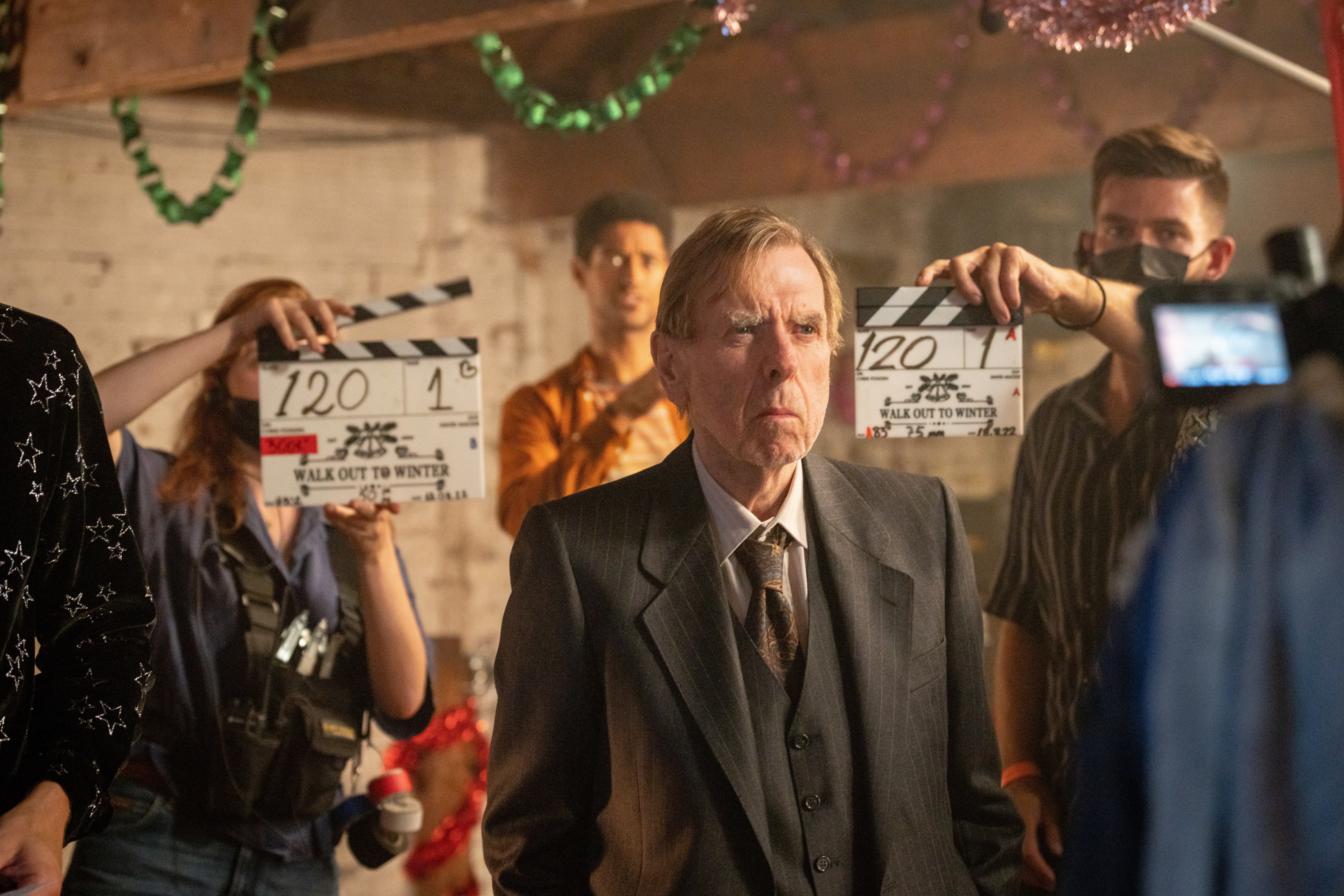 Actor stands in front of a camera while two people are holding clappers