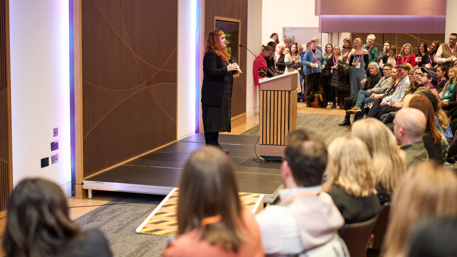 Michaela Mccaffrey stands at a podium in front of a seated audience giving a presentation