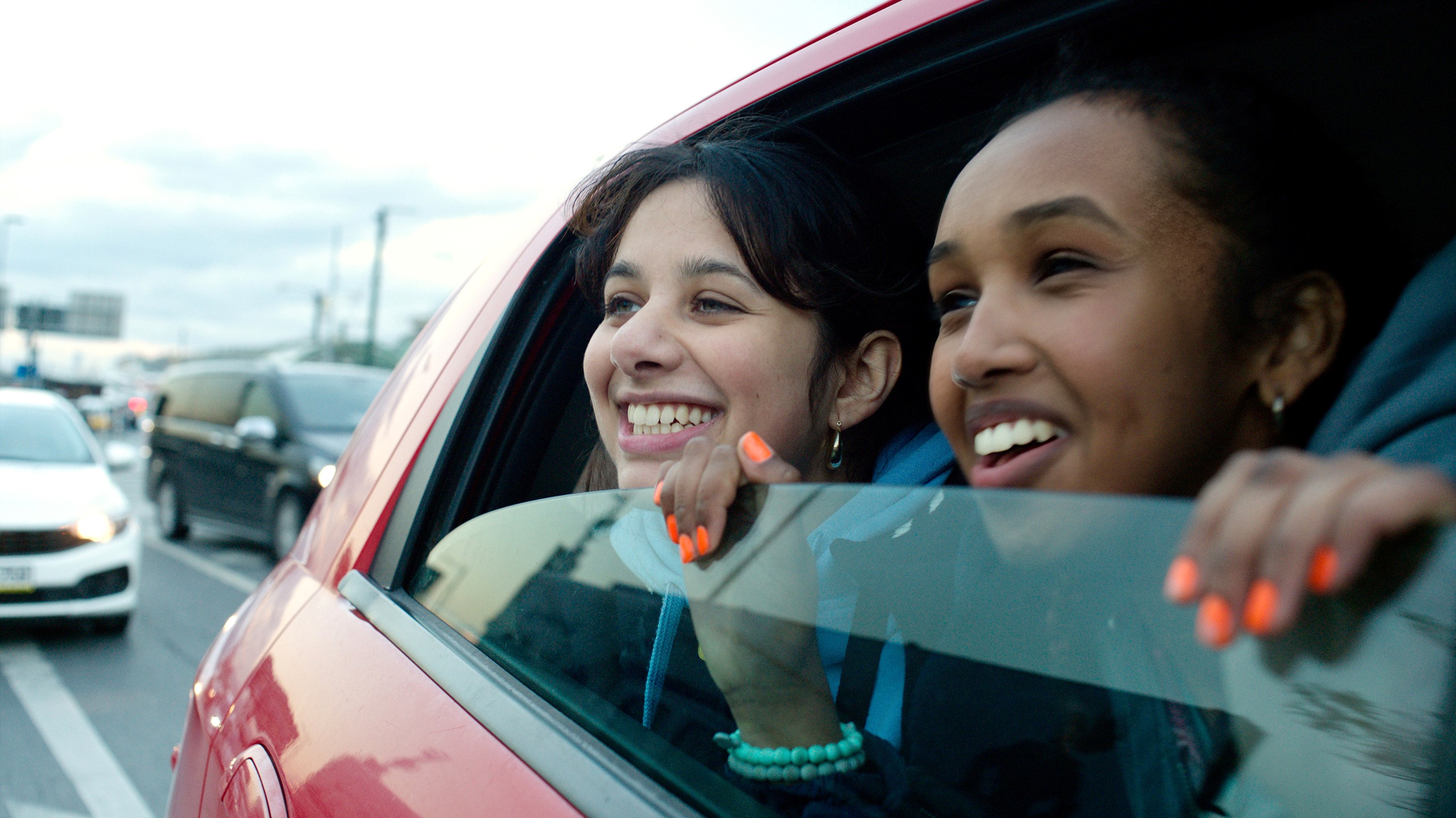 Production shot from Brides First of two girls looking out of a car window smiling