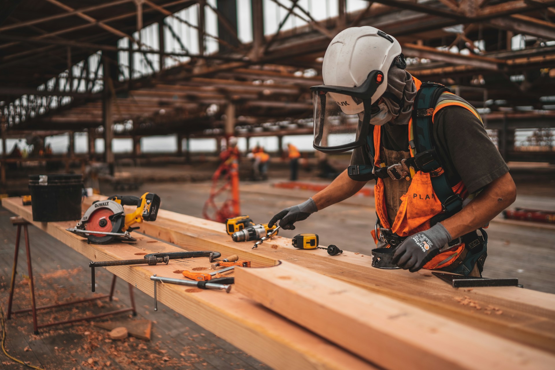 A carpenter using power tools to work with multiple long beams of wood