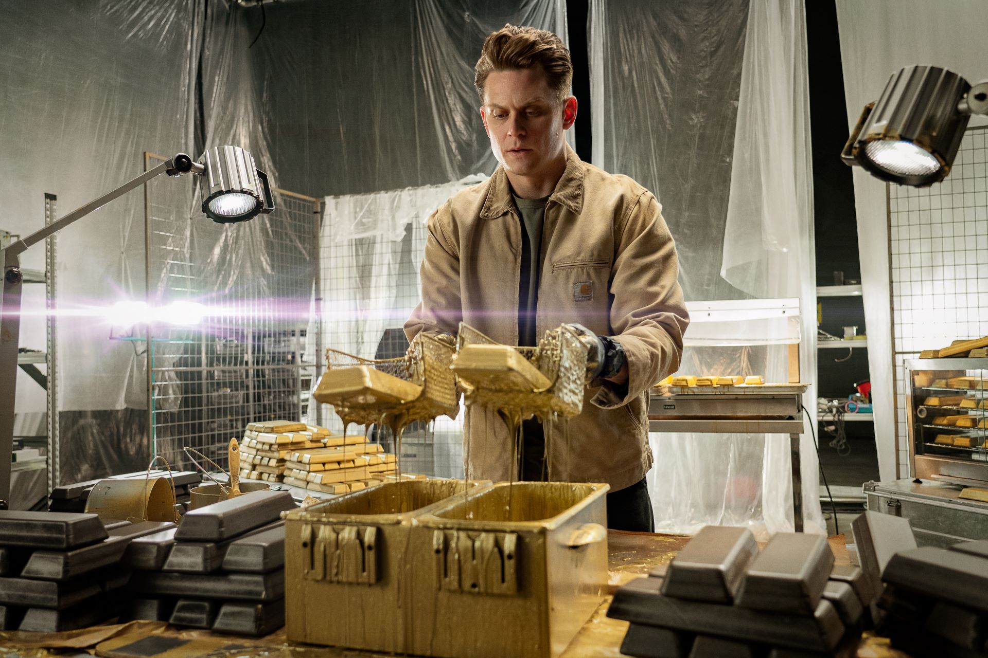 Billy Magnussen as Magnus holding dripping bars of gold on the set of Lift
