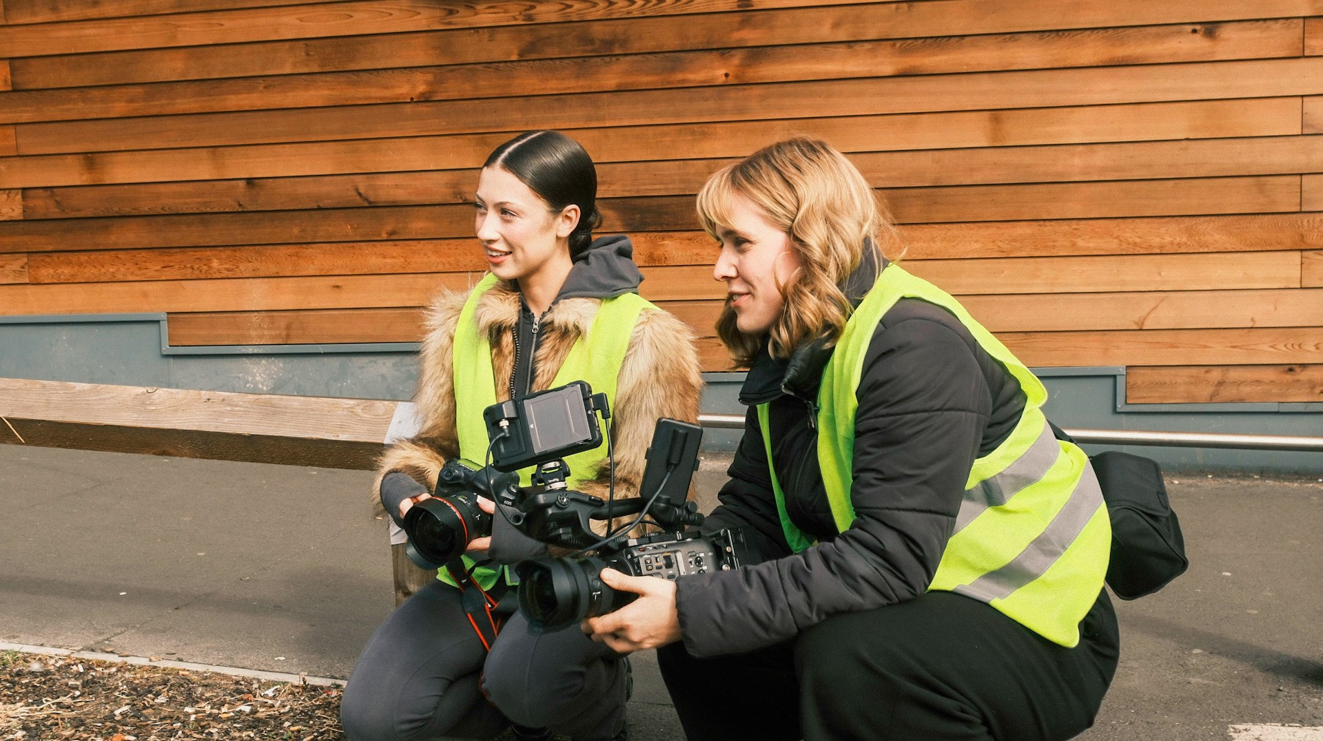 Two people hold camera equipment in high-vis jackets