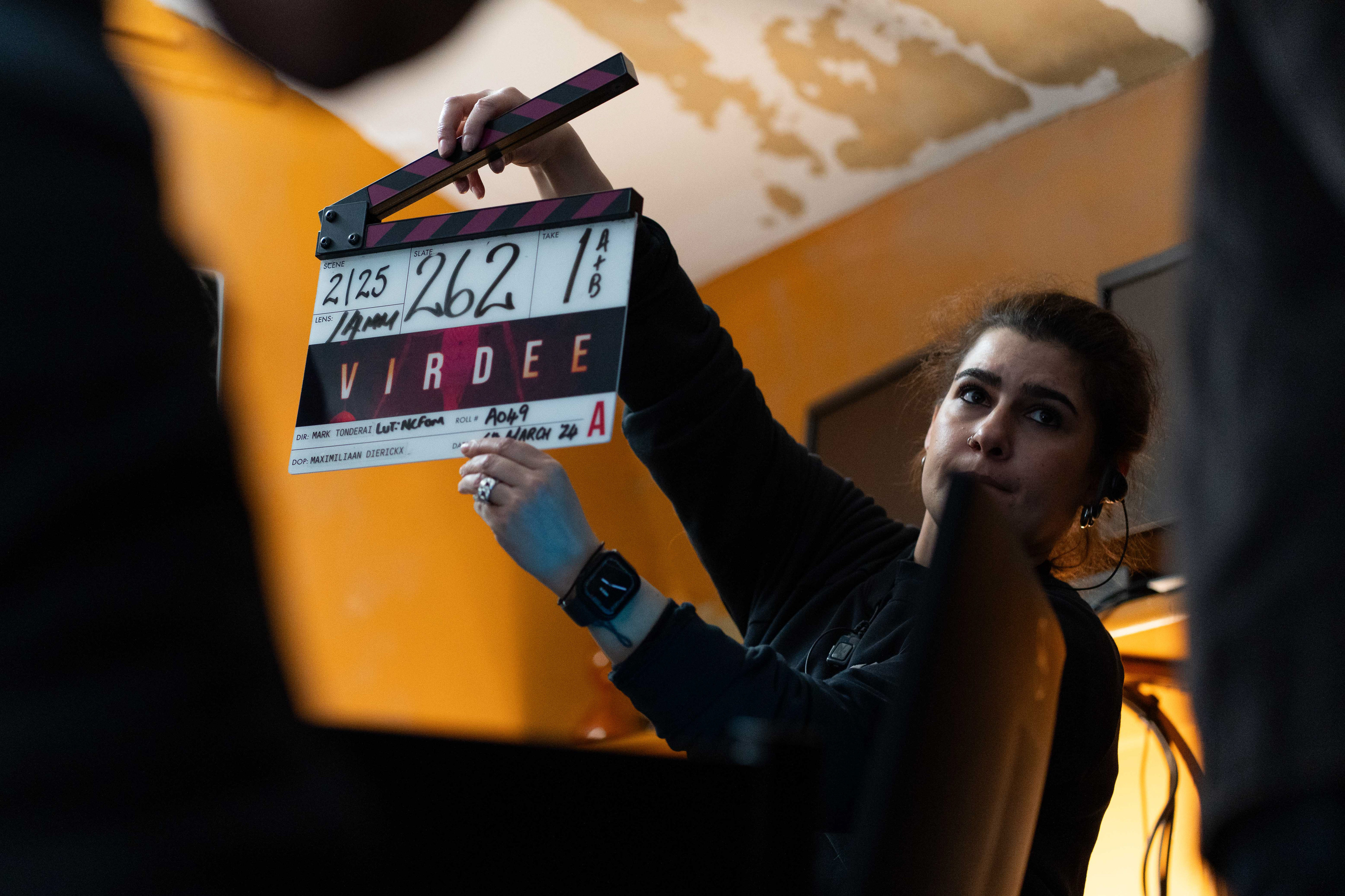 A BTS shot from Virdee. A person holds a clapperboard up to the camera.