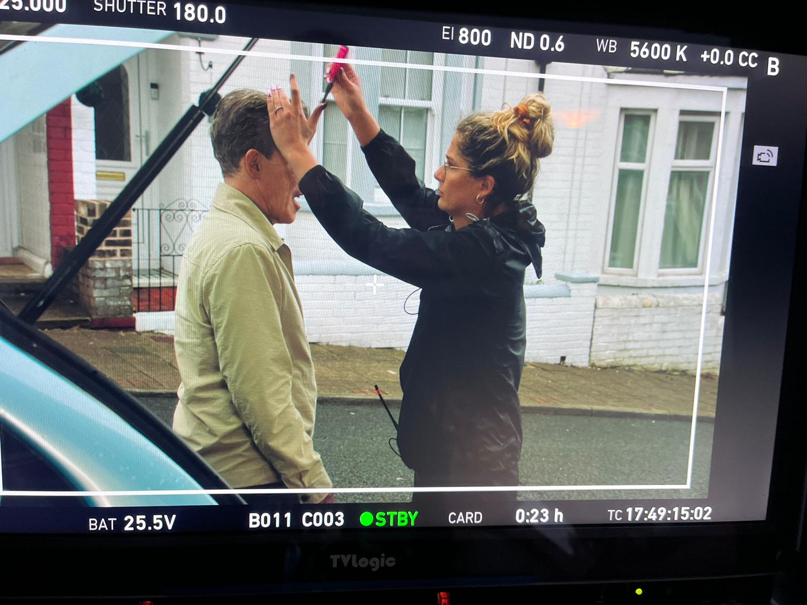 A hair and make-up artist fixes an actor's hair on set