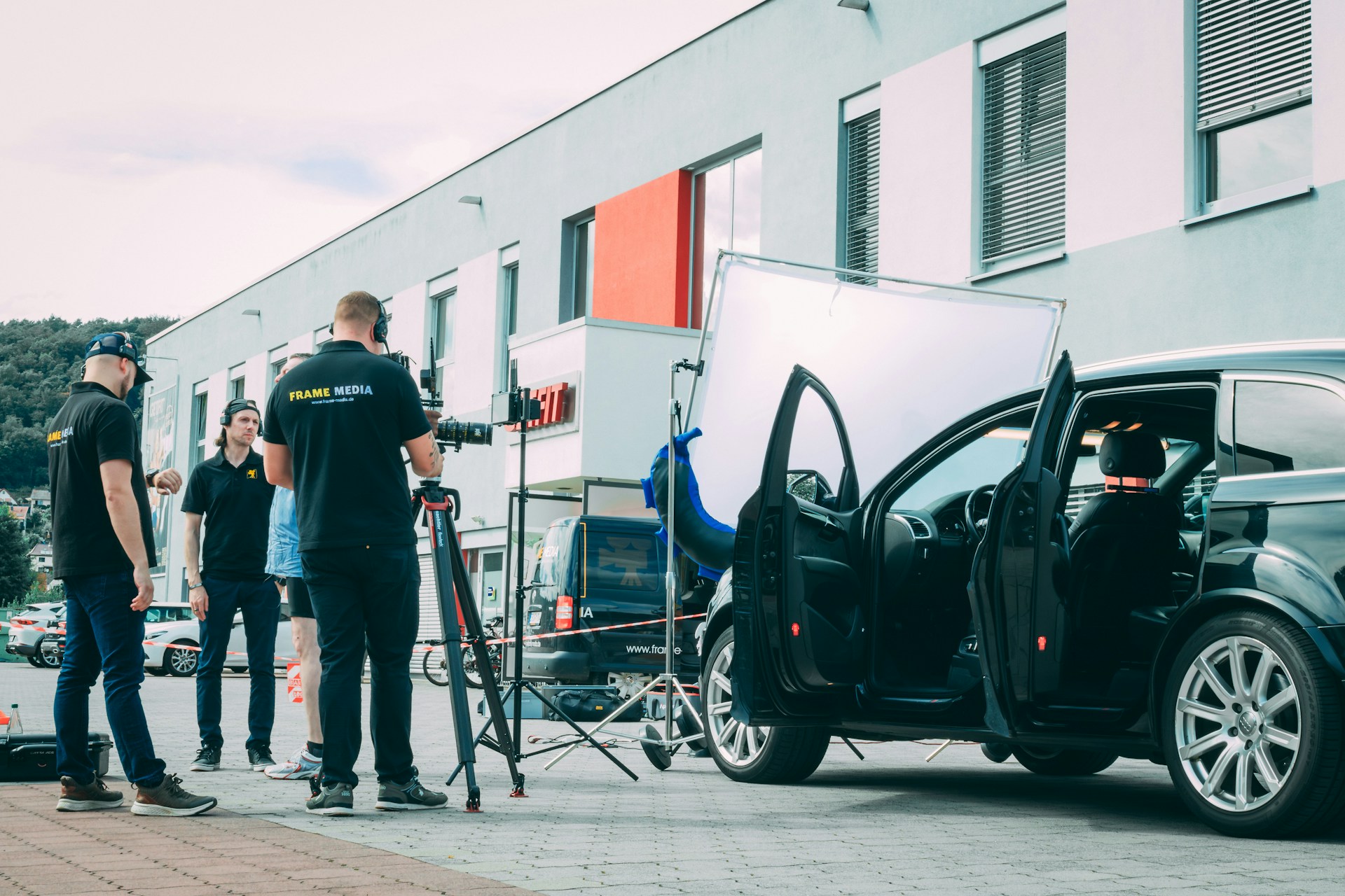 A team sets up an outdoor shoot with filming equipment and a car prop
