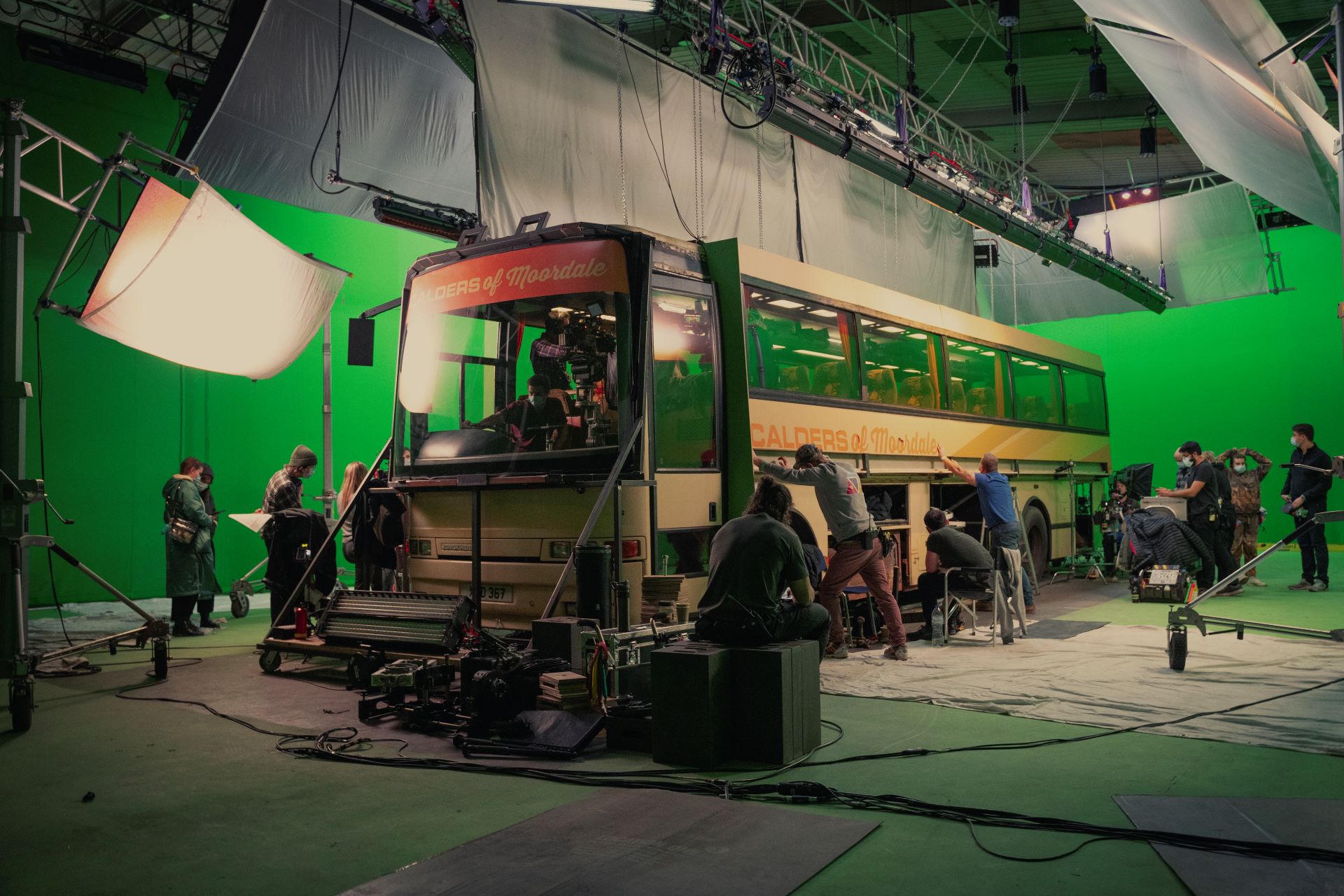 Behind-the-scenes of Sex Education season 3, production crew rig a large coach in front of a green screen with lights