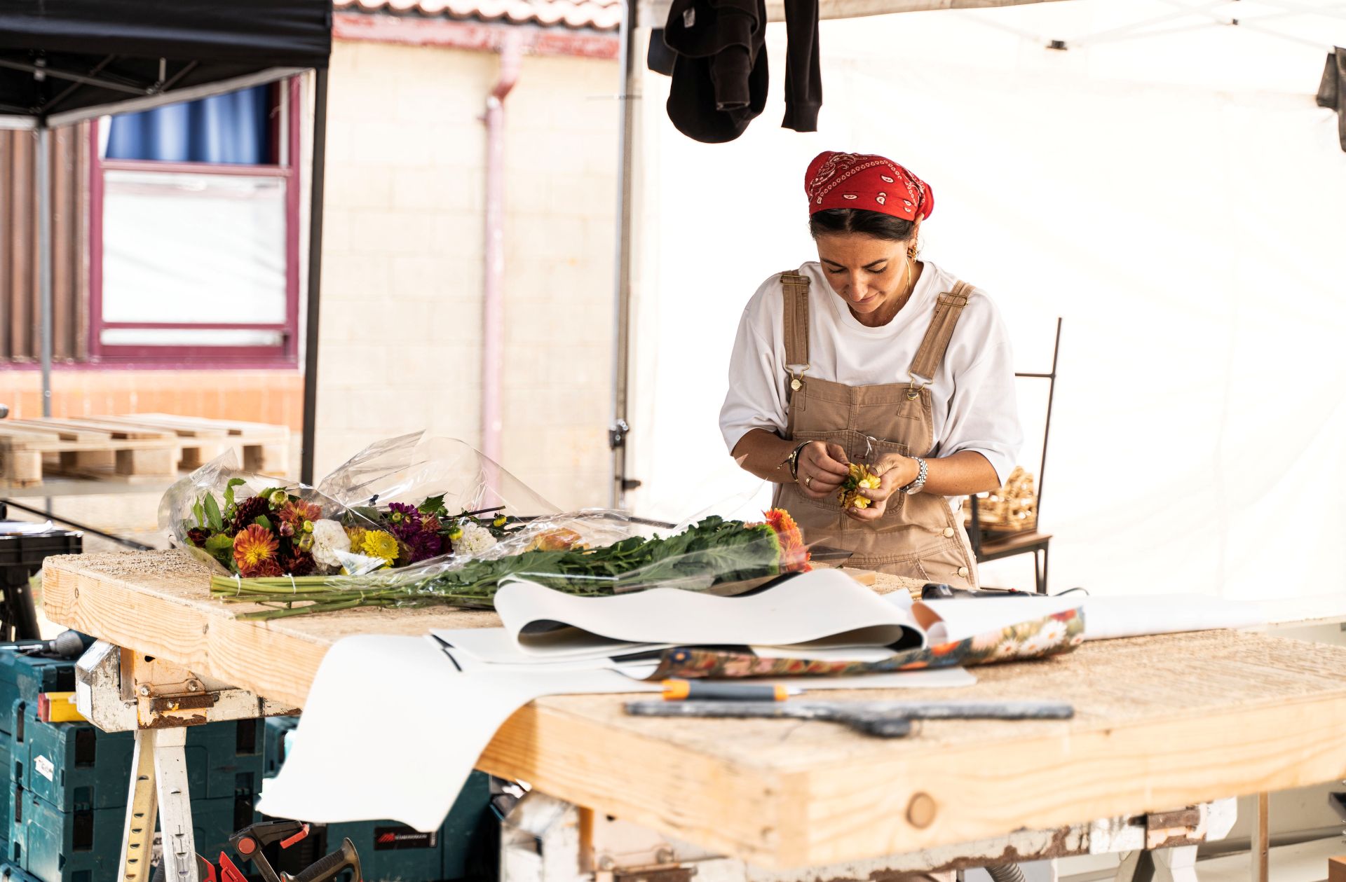 A person stands in an outdoor workshop, arranging flowers on a table top