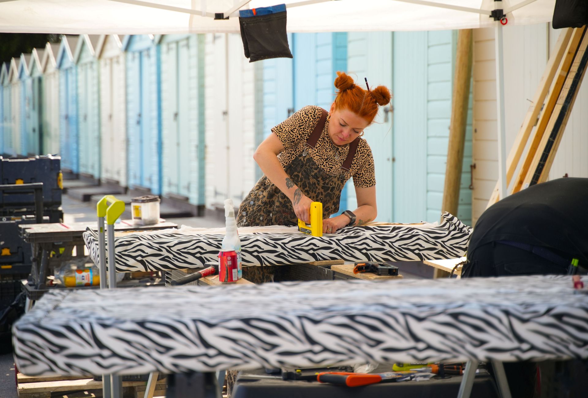 A person works in an outdoor workshop, stapling textiles onto wooden panels